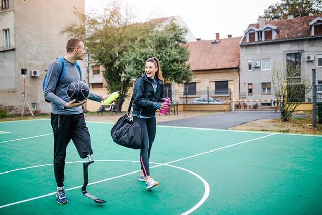 Two people, one with a prosthetic shin, cross a court following a game.