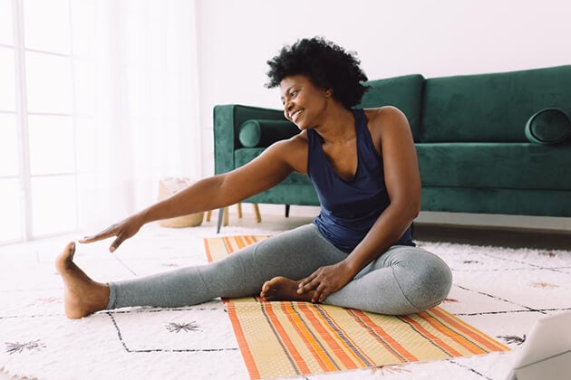 امرأة تمارس تمرينًا بسيطًا لإطالة العضلات المأبضية وعضلة الكتف أثناء الجلوس على الأرض.