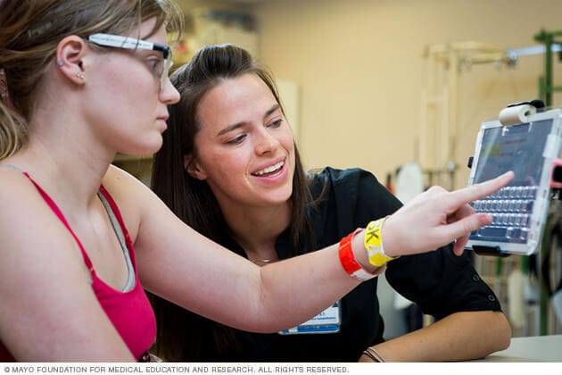 A young person interacts with a touch screen during a session with a physical therapist.