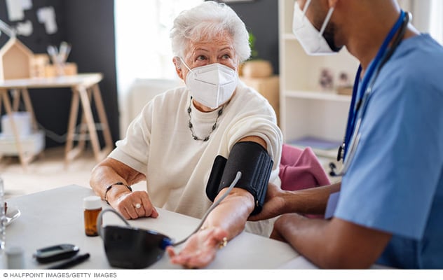 A person looks at a home care nurse who is taking a blood pressure measurement.