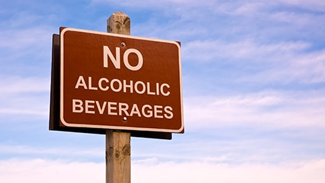 A sign prohibiting alcohol, with blue sky and clouds behind it