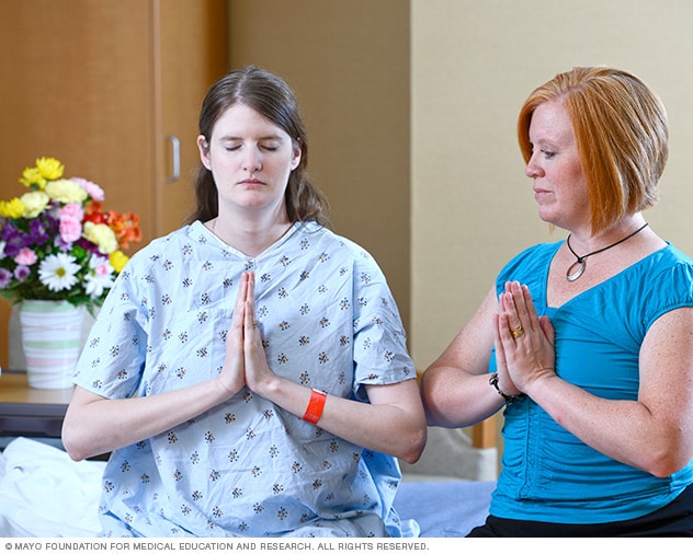 Two people have their hands clasped together in front of them to practice meditation